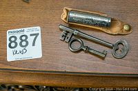 Vintage Schrader Universal tire pressure gauge with leather case and two vintage keys on wooden surface.