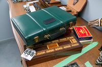Green leatherette closed backgammon set case, wooden cribbage board, and red/blue/white pool chalk box on table. Also shows part of worn vintage wooden toy truck.