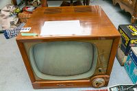 Front and top three-quarter view showing wood veneer cabinet, curved screen, ventilation slots on top and channel dial on front right.