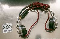 Front view of vintage headphones showing metal frame, black plastic ear cups, and red twisted fabric cord with plug.