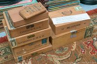 Stack of nine cigar boxes of various sizes shown with visible labels and partial text of brands including Benson & Hedges, Dunhill, and L. Goldsmith & Co.