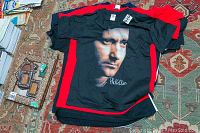 Multiple concert T-shirts stacked with visible front black Phil Collins shirt with portrait and signature