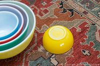 Four vintage Pyrex stacking mixing bowls nested together on a patterned rug, yellow bowl separate next to the stack.