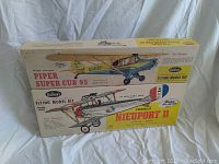 Two Guillows flying model kits stacked, boxes intact. Top box is Piper Super Cub 95 model, bottom is French Nieuport II model.
