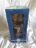 Side view of unopened boxed bobblehead through window showing figure face and uniform.