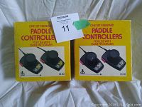 Pair of Atari CX30 paddle controllers in original yellow boxes with red text and Atari logos.
