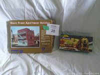 Boxes of Store Front Apartment Building model kit and Aherns train car model side by side showing brand and scale.