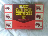 Top view of the wooden scale model construction kit box with brown and red color scheme, yellow text, and images of wooden vehicle models on sides.