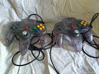 Two translucent purple Nintendo 64 controllers with cables coiled, showing front button layout and 3-prong design.
