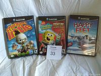 Photo showing front covers of three Nintendo Gamecube game cases: The Chicken Little Movie, SpongeBob SquarePants Creature from the Krusty Krab, and Happy Feet, with a lot number card in front of them.