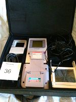 Full lot contents including Game Boy, Game Genie, carrying case, power adapter, and magnifier.