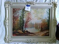 Frontal photo showing the full painting and its ornate cream/white frame with decorative floral detailing at corners and edges.