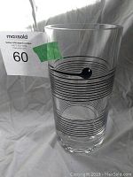 Clear cylindrical glass vase featuring black horizontal swirl lines and black glass droplet decoration inside, photographed front and top angles.
