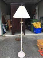 Full view of the floor lamp showing the round base, twisted column design, and conical white fabric lampshade in a storage garage.