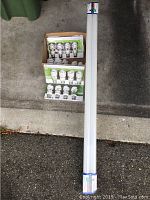 Box containing multiple packs of compact fluorescent bulbs and one 48 inch fluorescent tube bulb lying on floor.