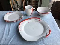 Photo showing one full 4-piece dining set: dinner plate, saucer, bowl, and mug with red and gray abstract accents.