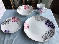 Front view of one complete four piece dining set showing plates, bowl, and mug with floral pattern.