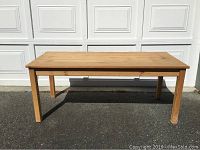 Full view of a rectangular solid pine wood coffee table against a garage door, showing the legs and natural wood finish.