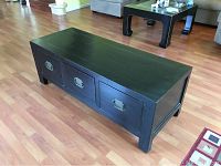 Front angle view of black cabinet table showing three drawers with metal handles.