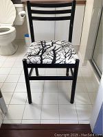 Front view of black wooden chair with tree-patterned seat cushion against bathroom background.