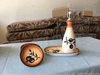 Six piece food oil set displayed on a table with ceramic cruet, drip tray and four dishes, showing olive design on each item
