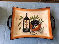 Rectangular ceramic serving dish with brown edges and painted design of olive oil bottle, olives, and garlic on front. Two handles on sides visible.