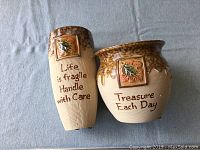 Two ceramic plant pots with inspirational quotes and leaf design, shown from front.