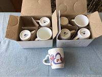 Photo showing two open boxes each containing four white ceramic tea cups, totaling eight cups. Cups are packed individually in separate compartments.