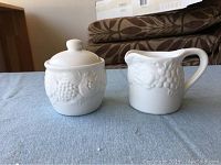 Milk and sugar set on blue fabric surface showing grapevine embossed design.