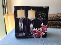 Box front showing two crystal candleholders holding pillar candles, floral design and product info visible