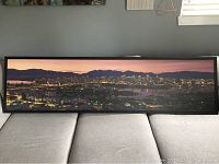 Wide shot of matte panoramic picture of Vancouver skyline in black frame laid on a grey couch.