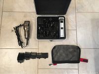 Both hair clippers with attachments, cords, and zippered mesh pouches laid out on a tiled floor.