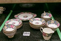 Wide angle view of the tea service set with teacups, saucers, dessert plates, and creamer on black countertop