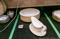 Stack of fine bone china dinner plates with gold vine-like pattern near rim, next to a matching gravy boat and underplate with the same design.