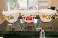 Front view of three Fire King milk glass bowls showing fruit motifs on each bowl.