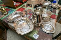 Wide view showing silver-plated serving bowls, candle stick holders, vase, and platters arranged on a table.