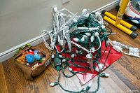 Collection of tangled Christmas string lights including larger bulbs and smaller decorative lights, cords manually coiled.