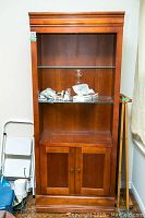 Straight-on view of the wooden bookcase showing the glass shelf, upper open shelf and lower cabinet with doors.