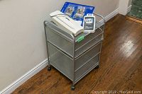 Metal cabinet with mesh drawers on casters, items including two printer cartridges and shredder placed on it