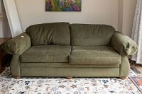 Front view of green fabric upholstered sofa with cushions and wooden feet.