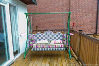 Front view of green A-frame swing with seat and cushions on wooden deck