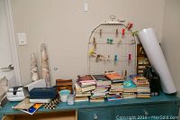 Wide shot showing a variety of items for sale including stacks of books, decorative birdcage with colorful clips, and other objects on a piece of furniture.