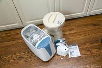 Photo of all three items together on a wooden floor: Honeywell humidifier, Infinity pet food dispenser, Waterpik device and manual.
