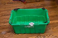 Top-side view of a green rectangular plastic basket showing black reinforced corners and handles on the sides