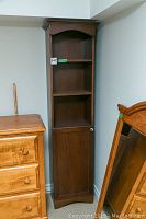 Full view of the tall wooden cabinet alongside other furniture. The cabinet features two open shelves and a lower enclosed section with door.
