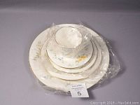 Full 5 piece place setting wrapped with plastic showing stacked plates and cup