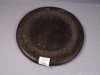 Top view of the round dark wood table top showing carved geometric border