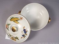 Top-down view of open porcelain covered vegetable casserole dish showing interior and lid with fruit and vegetable pattern and gold knob.