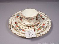 Full place setting stacked showing dinner plate, luncheon plate, bread and butter plate, coffee/tea cup, and saucer with floral and gold rim details.