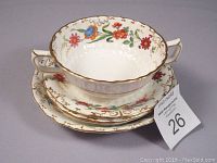 Porcelain set including cream soup bowl on top of saucers and bowls, showing floral patterns and gold rim